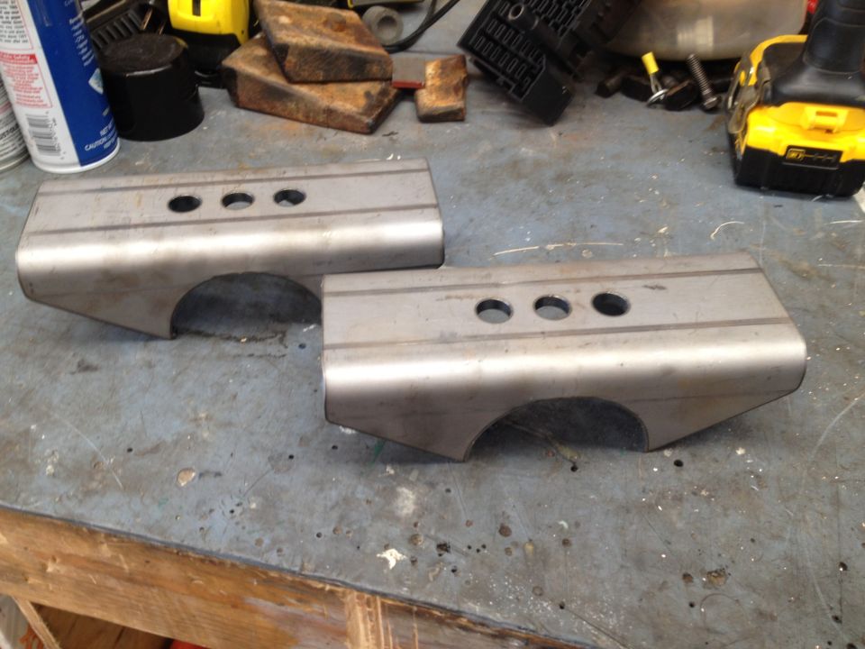 Two custom steel suspension parts with three holes on a workbench.
