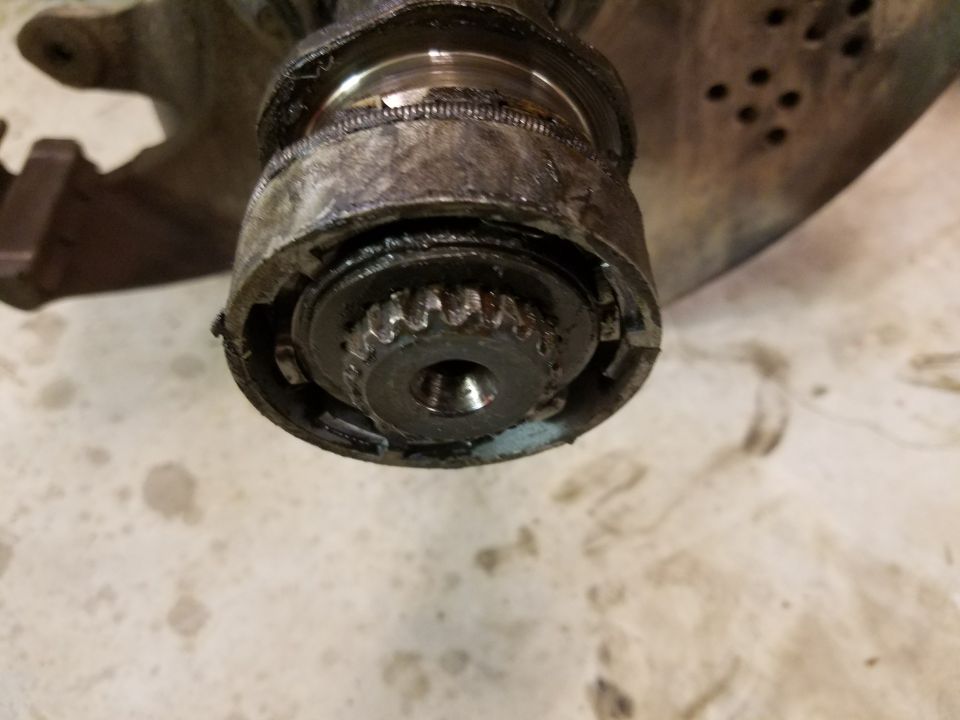 Close-up of a greased and worn splined shaft with a gear and damaged housing.
