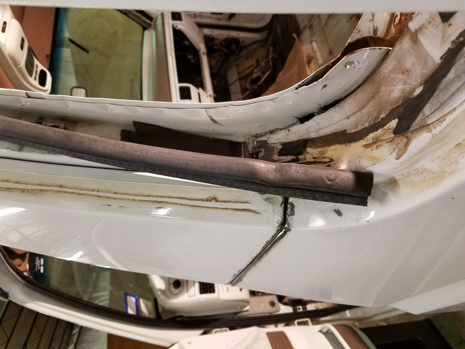 Close-up of damaged white vehicle door jamb with rust and a rubber seal.
