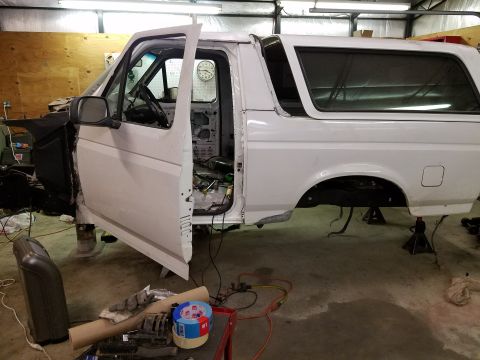 1996 Ford Bronco - A white Ford Bronco is in a garage, undergoing restoration. The driver's side door is open, revealing the interior, and the vehicle is supp…