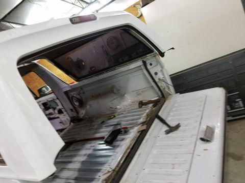 1996 Ford Bronco - The interior of a white pickup truck bed and cab is shown from a rear-facing angle. Tools, including a hammer, are scattered in the bed, an…