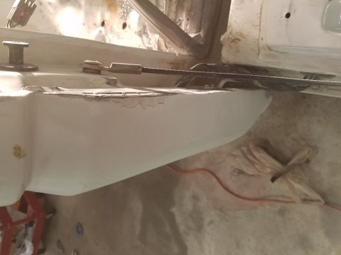 1996 Ford Bronco - A close-up view of a white automotive body panel with a rough, unfinished edge, likely undergoing repair or modification. A metal cable and…