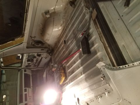 1996 Ford Bronco - The interior of a vehicle is being worked on, with tools and a broom laid out on the ribbed metal floor. The driver's side door and dashboa…