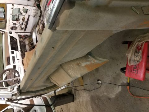 1996 Ford Bronco - A close-up, angled view of the lower body panel and exhaust pipe of a white vehicle, possibly a 1996 Ford Bronco, in a workshop setting. Th…