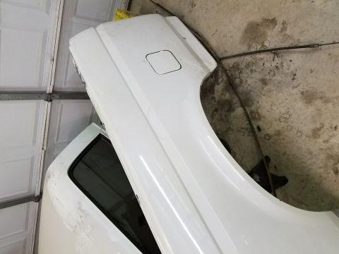 1996 Ford Bronco - A white Ford Bronco fender and part of a door are leaning against a garage wall. The fender has a fuel filler door and the door has a dark…