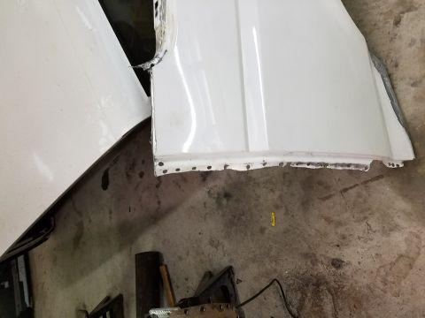 1996 Ford Bronco - A white vehicle fender is shown in a workshop setting. The fender has been cut and has visible drill holes along the bottom edge, indicatin…