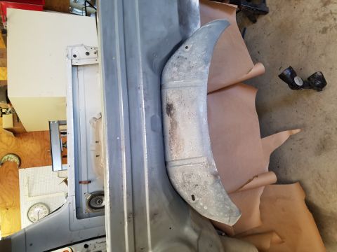1996 Ford Bronco - A curved, metallic part, possibly a fender liner or splash guard, rests on brown paper next to a partially disassembled vehicle frame. The…