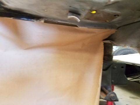 1996 Ford Bronco - The underside of a vehicle is shown, with brown paper covering a section of the frame. A green metal bracket and part of a tire are visible…
