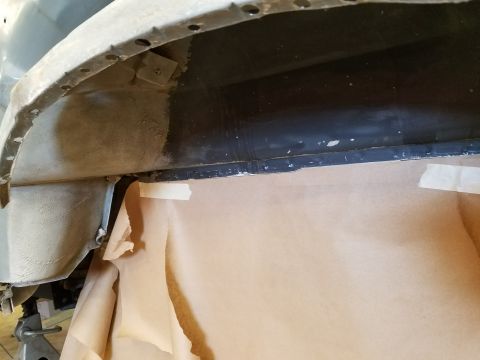 1996 Ford Bronco - Close-up view of the underside of a vehicle's wheel well area, showing metalwork, some black undercoating, and brown paper masking. A porti…