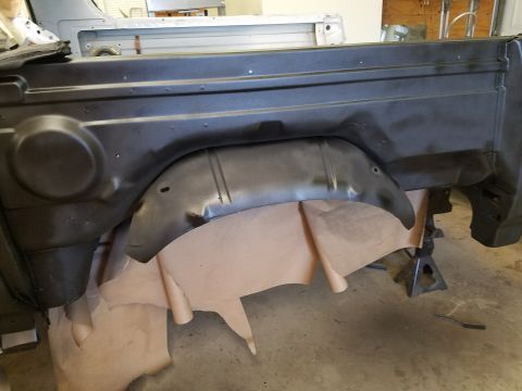 1996 Ford Bronco - The interior of a vehicle's rear wheel well is visible, lined with brown paper and supported by jack stands.
