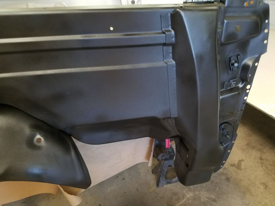 Close-up of a black painted vehicle body panel, possibly a fender well area, with a jack stand visible underneath
