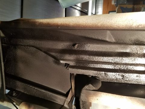 1996 Ford Bronco - Close-up view of the underbody of a vehicle, showing a dark protective coating applied to the frame and structural components.