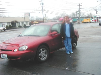 1997 Ford Taurus - A woman stands next to a red 1997 Ford Taurus on a wet day.