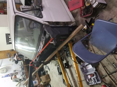 1996 Ford Bronco - A white 1996 Ford Bronco is undergoing repairs in a cluttered garage, with its front end dismantled.