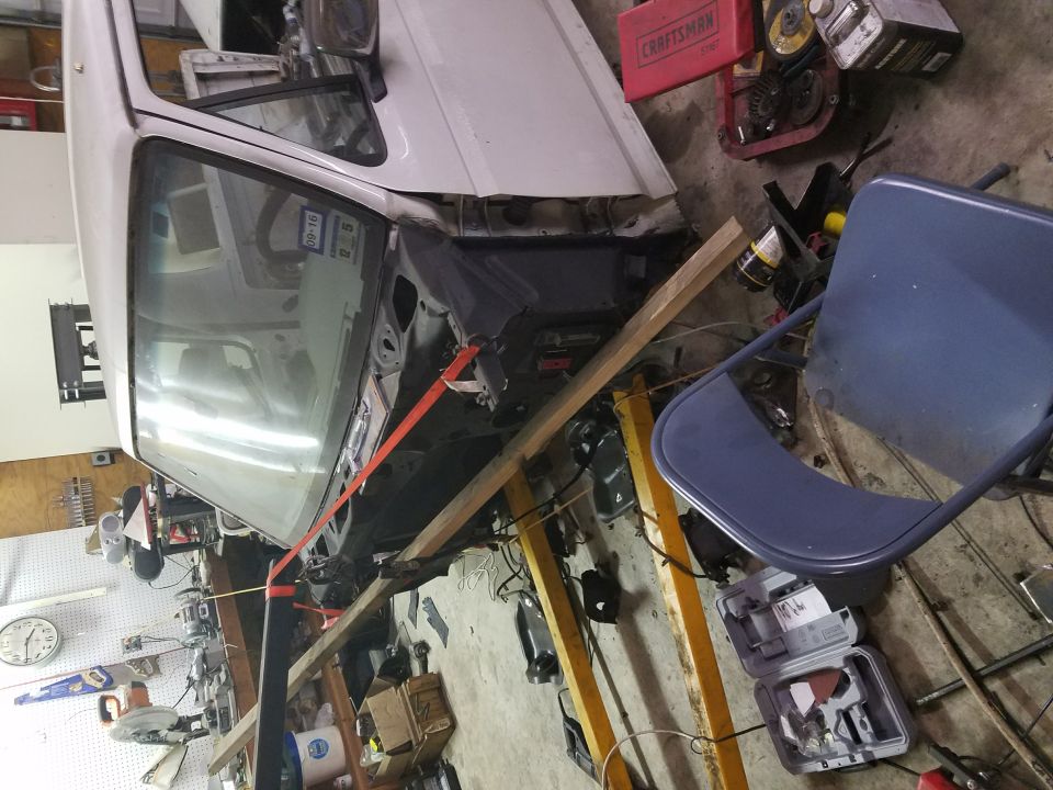 White 1996 Ford Bronco front end disassembled in garage, supported by wooden beams