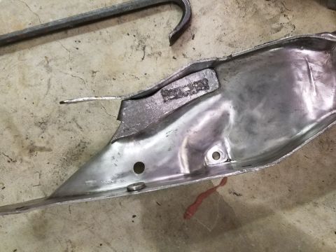 1996 Ford Bronco - A metal component with stamped markings is shown on a concrete surface, with a hook tool in the background.