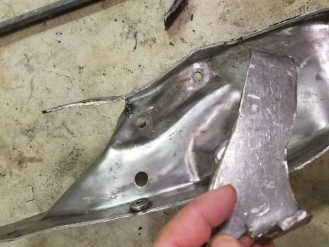 1996 Ford Bronco - A hand holds a metal piece against a damaged metal bracket, possibly for repair or inspection.