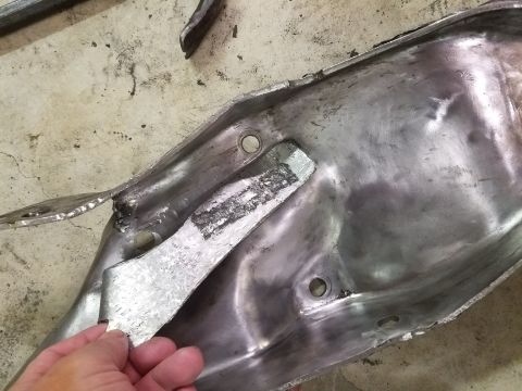 1996 Ford Bronco - A hand holds a damaged metal part, possibly from a vehicle, on a concrete floor.