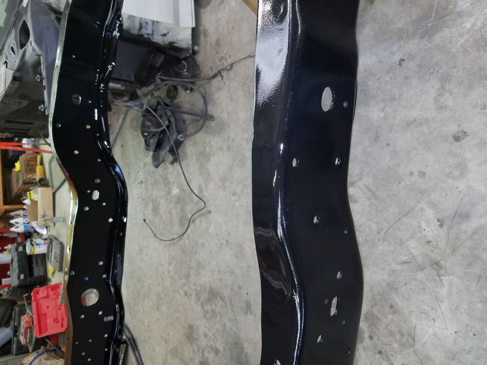 Two black painted vehicle frame rails with numerous holes
