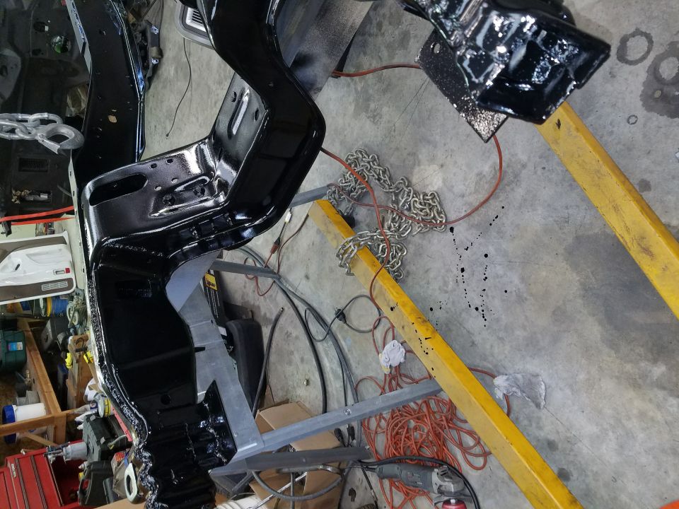 Black painted vehicle frame on a yellow engine hoist with chains and tools