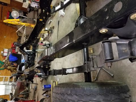 1996 Ford Bronco - The chassis and suspension components of a vehicle are visible, including leaf springs and a tire, in a workshop setting.