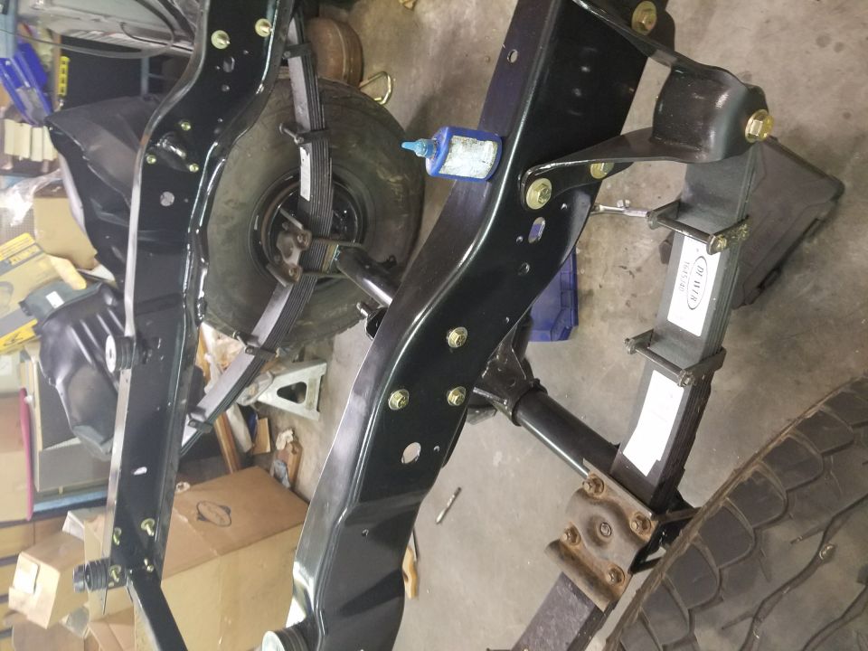 Close-up of a vehicle's black frame with leaf springs and tires visible