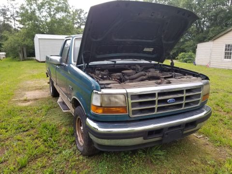 1996 Ford F-150 - A teal Ford F-Series truck sits in a grassy yard with its hood open, revealing the engine.