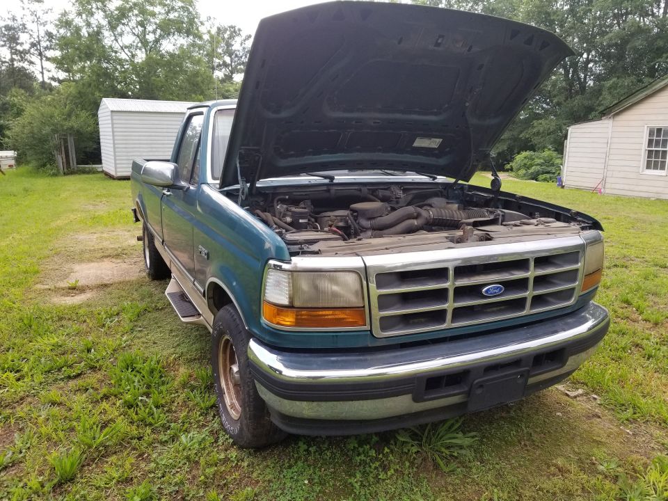 Teal Ford F-Series truck with hood open, showing engine bay. Grille has horizontal bars and a Ford emblem