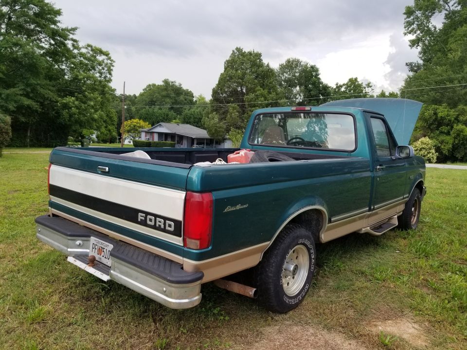 Green and tan Ford F-150 pickup truck, rear-left view, hood open, some items in bed