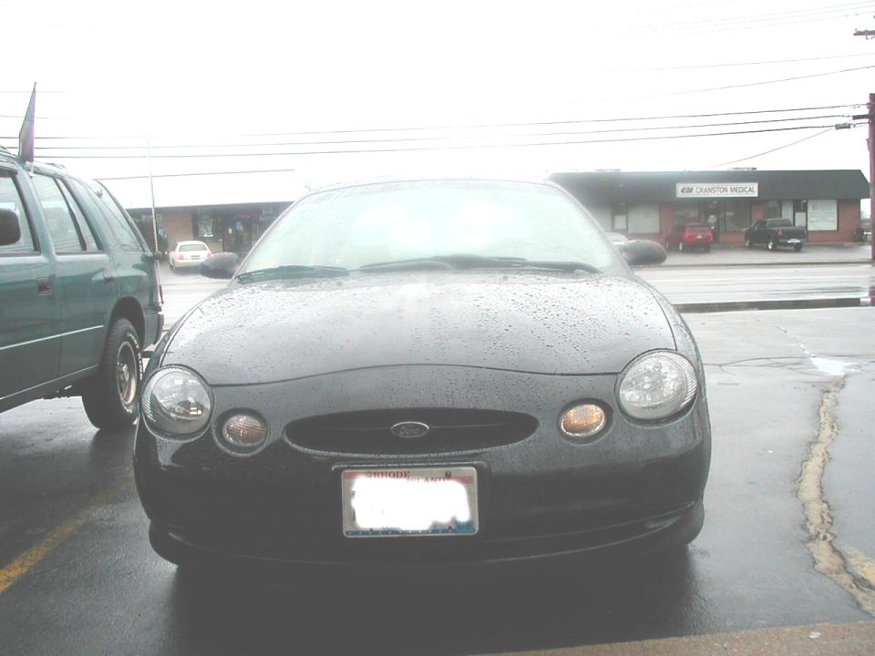 Front view of a dark 1997 Ford Taurus with a green SUV to its left