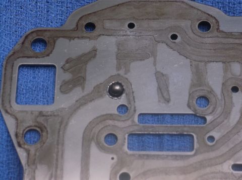 1979 Ford Ranchero - Close-up of a metal gasket showing oil residue and a small ball bearing within a circular recess.