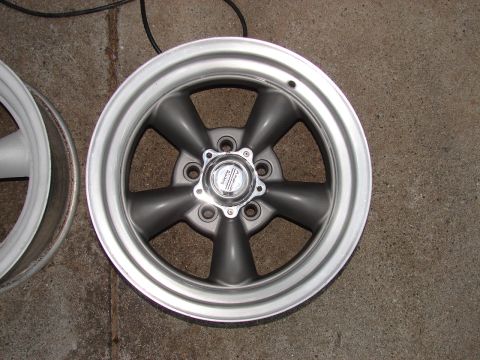 1973 Ford Ranchero - A single gray five-spoke car wheel with a chrome center cap is shown on a concrete surface.