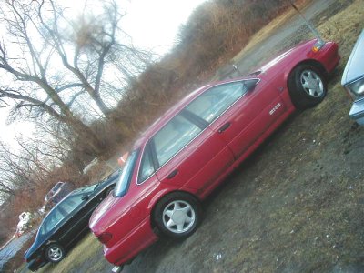 1997 Ford Taurus - A red sedan is parked on a grassy slope next to another vehicle, with a Supermotors logo in the corner.