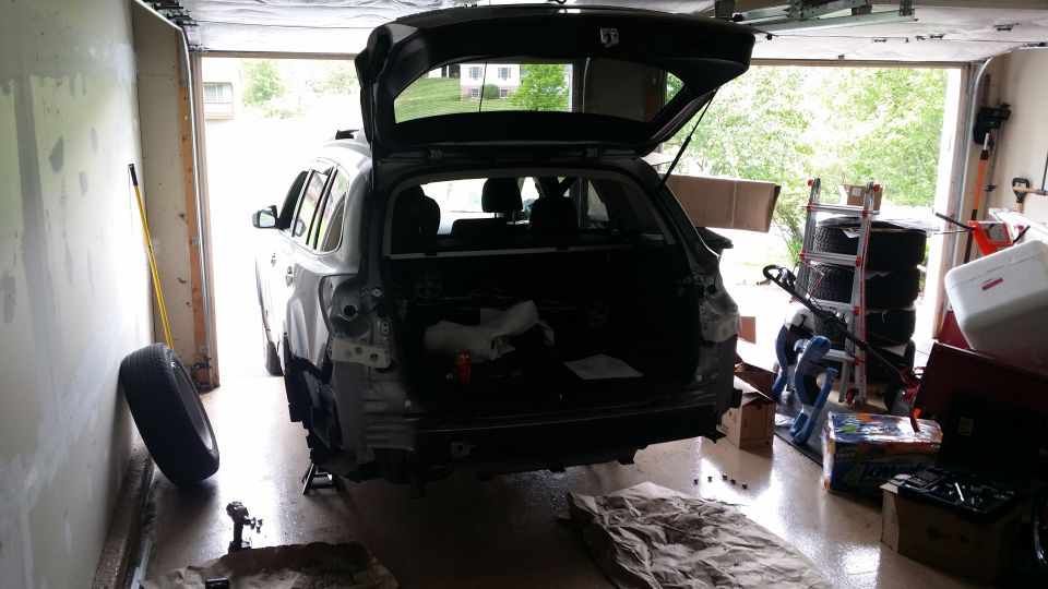 Gray Subaru Outback with rear bumper removed, parked in a garage with the trunk open