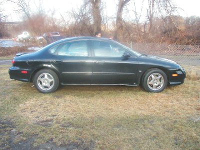 1997 Ford Taurus - This 1997 Ford Taurus is seen from the side, parked on a grassy area with trees in the background.