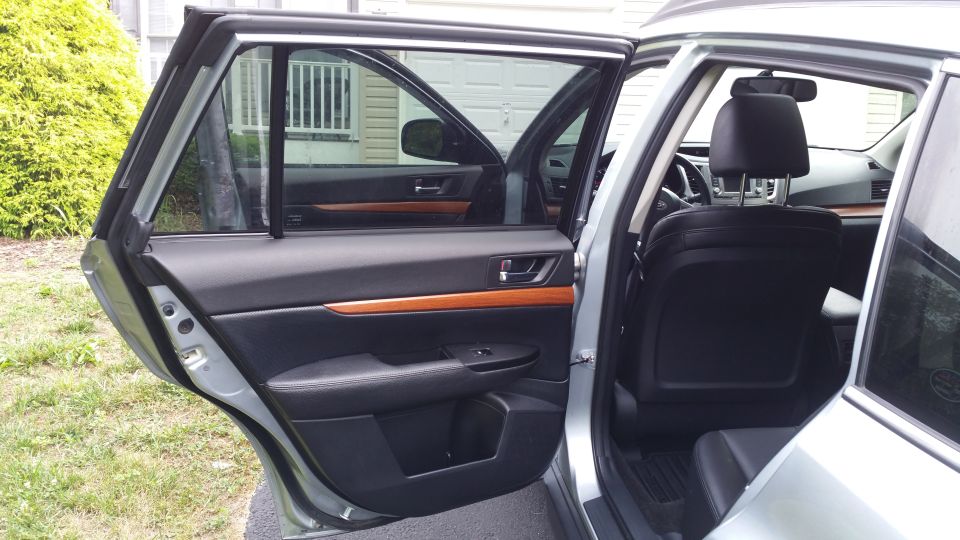 Silver Subaru Outback interior with open rear door, black leather seats, and wood trim