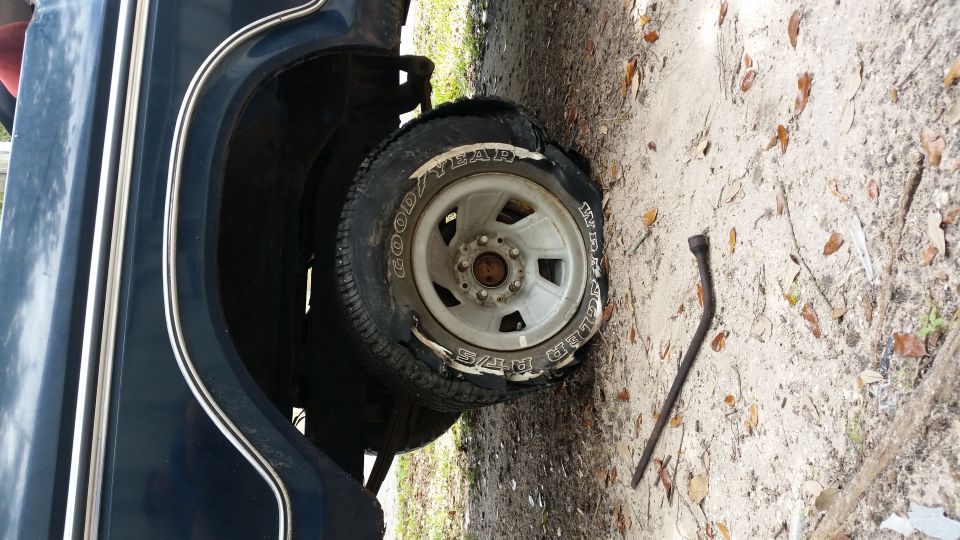 Flat tire on a dark blue vehicle with a jack lying on the ground next to it
