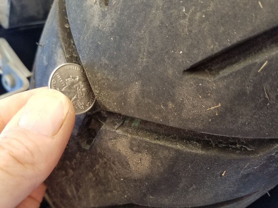 Quarter inserted in worn motorcycle tire tread groove to check depth