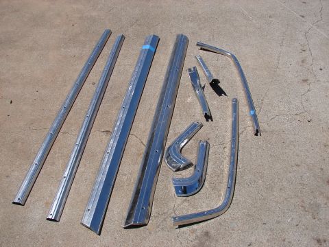 1973 Ford Ranchero - Various chrome trim pieces, possibly for a classic car, are arranged on a concrete surface.