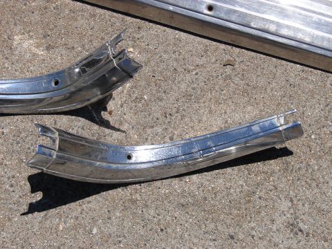 1973 Ford Ranchero - Two damaged chrome trim pieces lie on a concrete surface, possibly from a vintage vehicle.