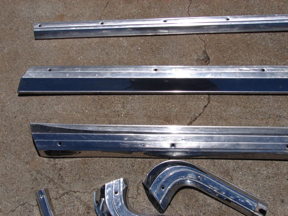 Several chrome trim pieces, including long strips and curved sections, laid out on a concrete surface