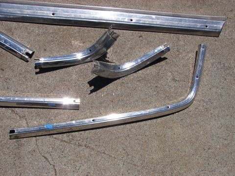 1973 Ford Ranchero - Several pieces of chrome trim, likely for a vehicle, are laid out on a concrete surface. The parts show signs of wear and have pre-drilled…