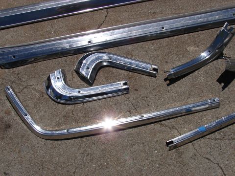 1973 Ford Ranchero - Collection of chrome trim pieces, likely for a classic car, scattered on a concrete surface.
