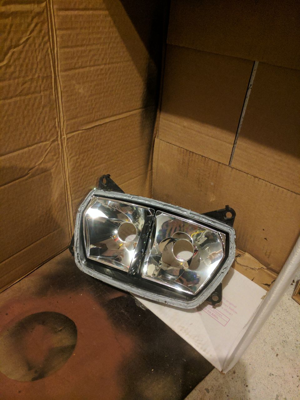 Motorcycle headlight assembly with dual clear lenses, mounted on a cardboard background