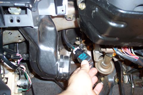 1993 Toyota Pickup/SR5 - Close-up of a hand holding a blue relay near the dashboard wiring and steering column of a vehicle.