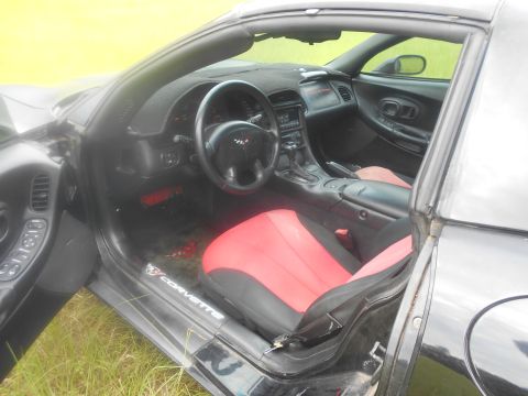 1992 Ford Bronco - The interior of a black sports car, red seats and 'Corvette' badging on the door sill, is visible.