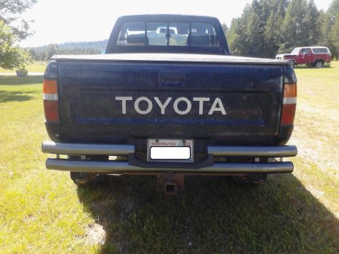 1993 Toyota Pickup/SR5 - A dark blue Toyota pickup truck is parked in a grassy area with another red vehicle in the background.