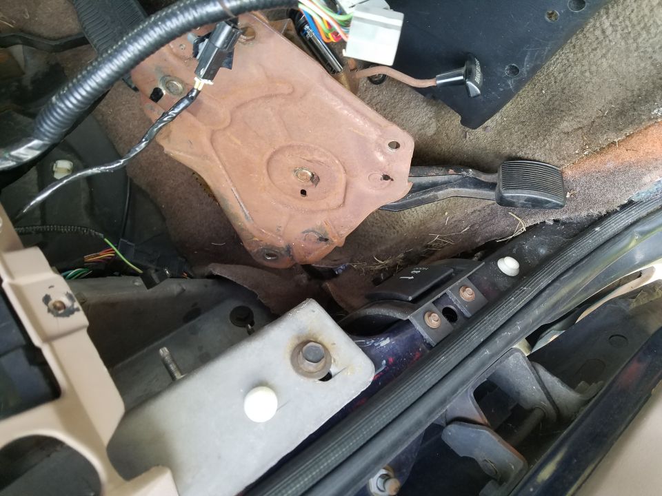 Vehicle interior floor showing pedals, rusty bracket, and wiring harness