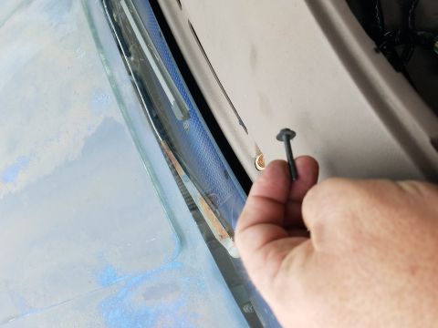 1994 Ford Bronco - A hand holds a screw near the windshield trim of a vehicle, with interior components visible.