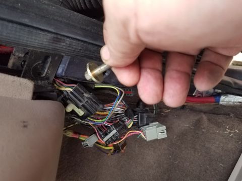 1994 Ford Bronco - A hand removes a bolt from a vehicle's interior wiring harness, revealing multiple connectors and wires.